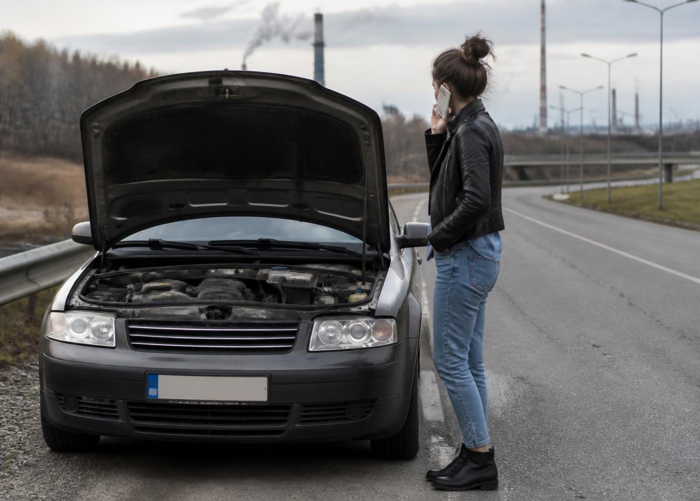 Driver standing beside a stopped car with the hood raised, phone to ear