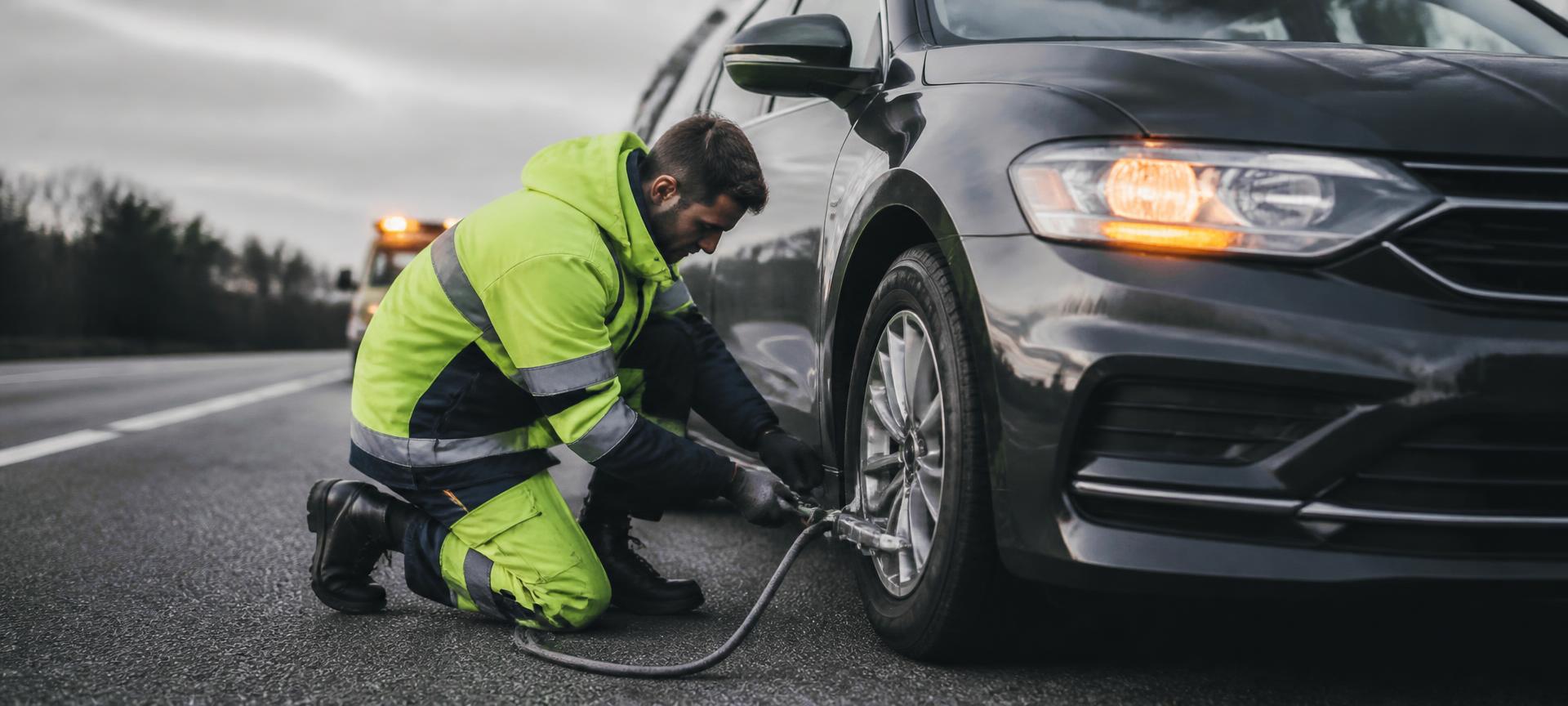 Service operator kneeling at a car's front wheel on the road shoulder